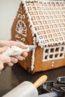 Hands decorating gingerbread house with icing — Stock Photo