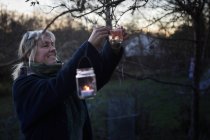 Reife Frau schmückt Baum mit Teelichtern — Stockfoto