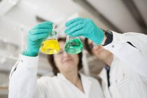 Женщины-ученые держат конические колбы с желтыми и зелеными жидкостями — стоковое фото
