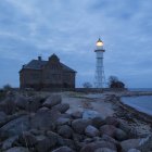 Освітлений маяк і будівлі на пляжі в сутінках — стокове фото