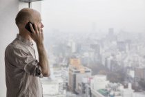 Чоловік розмовляє по телефону і дивиться через вікно — стокове фото