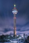 Torre de comunicaciones iluminada por la noche en el cielo nublado - foto de stock