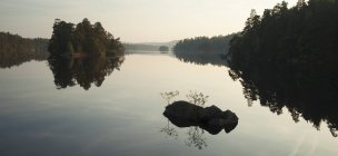 Silhouetted trees and rocks reflections in lake water — Stock Photo