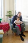 Uomo anziano seduto in poltrona e tenendo nipote in grembo — Foto stock