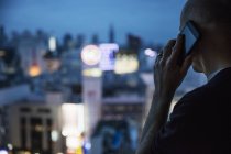 Homem falando ao telefone e olhando pela janela à noite — Fotografia de Stock