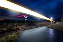 Sentieri luminosi di passaggio del treno e segnali di avvertimento di notte — Foto stock