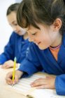 Duas meninas escrevendo em sala de aula, foco em primeiro plano — Fotografia de Stock