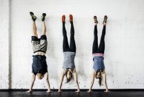 Les jeunes femmes et l'homme pratiquant handstand dans la salle de gym — Photo de stock