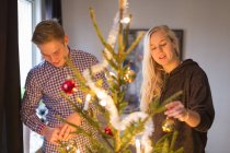 Vista lateral de pareja decorando árbol de navidad juntos - foto de stock