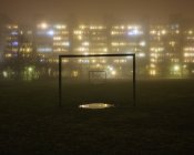 Edifici residenziali illuminati con campo da calcio in primo piano nella nebbia — Foto stock