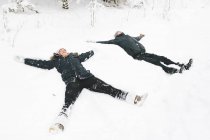 Молодая пара делает снежных ангелов зимой — стоковое фото
