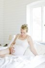 Pregnant mid-adult woman sitting on bed — Stock Photo