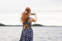 Вид ззаду молода жінка фотографує море — стокове фото