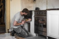Homem maduro reparando forno tradicional na cozinha — Fotografia de Stock
