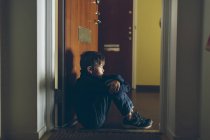 Мальчик сидит на полу рядом с дверью, дифференциальный фокус — стоковое фото