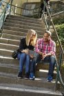 Mann und Frau sitzen nebeneinander auf Stufen und schauen auf digitales Tablet — Stockfoto