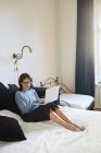 Женщина сидит на кровати и с помощью ноутбука — стоковое фото