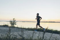 Вид сбоку взрослого мужчины средних лет, совершающего пробежку на берегу моря — стоковое фото