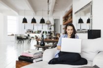 Женщина за компьютером с концентрацией внимания в гостиной — стоковое фото