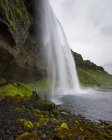 Hiker looking up at Seljalandsfoss waterfall, blurred motion — Stock Photo