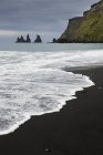 Formations rocheuses et sable noir sur la plage par falaise — Photo de stock