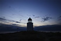 Lighthouse silhouetted at cloudy sunset sky — Stock Photo