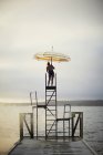 Женщина с зонтиком, стоящая на лестнице у озера — стоковое фото