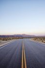 Strada deserta vuota con catena montuosa al tramonto — Foto stock