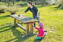 Mother with daughter oiling wooden table in garden — Stock Photo