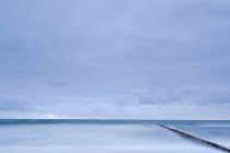 Larga exposición tiro de paisaje marino con rompeolas bajo el cielo malhumorado - foto de stock
