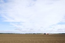 View of agricultural field with distant working tractor — Stock Photo