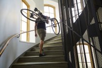 Вид сзади велосипедиста, несущего велосипед по ступенькам — стоковое фото