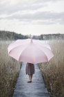 Woman with pink umbrella standing on wooden pier — Stock Photo