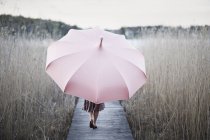 Mulher com guarda-chuva andando no cais de madeira — Fotografia de Stock