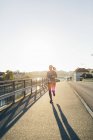 Young woman jogging on bridge in backlit — Stock Photo