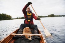 Человек смотрит прочь с собакой в каноэ на озере — стоковое фото