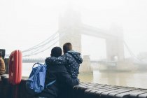 Mittlerer erwachsener Mann hält Jungen beim Anblick einer Tower Bridge in London im Nebel — Stockfoto