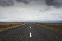 Road stretching through dry landscape under cloudy sky — Stock Photo