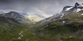 Gama de jotunheimen y exuberante valle verde con arco iris en el cielo - foto de stock