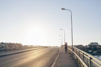 Молода жінка біжить на мосту в яскравому сонячному світлі — стокове фото