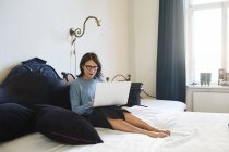 Mulher adulta usando laptop enquanto sentado na cama — Fotografia de Stock