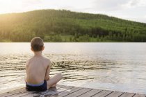 Menino sentado à beira do lago, foco seletivo — Fotografia de Stock