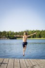 Visão traseira do menino pulando na água do molhe — Fotografia de Stock