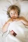 Portrait of blonde girl wearing headphones while lying in bed — Stock Photo