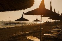 Strand mit Strohschirmen und Liegestühlen bei Sonnenuntergang — Stockfoto