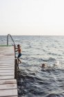 Side view of brother swimming while sister climbing ladder — Stock Photo