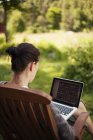 Mulher usando laptop no jardim, foco em primeiro plano — Fotografia de Stock
