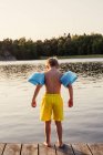 Rückansicht eines Jungen mit Wasserflügeln, der am Steg steht — Stockfoto