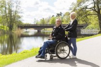 Uomo sulla sedia a rotelle con assistente personale nel parco — Foto stock