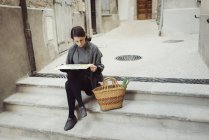 Joven turista sentado en los escalones y mirando el mapa - foto de stock